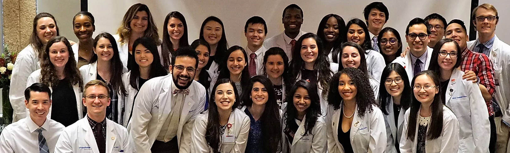 Group of young people in lab coats smiling, with Gold Humanism Honor Society written over them