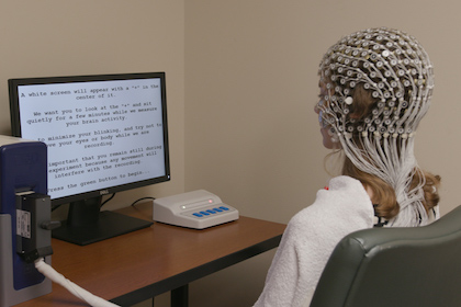 Woman sits at a monitor with electrodes covering her head