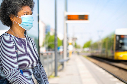 A Black woman at a train station wearing a mask