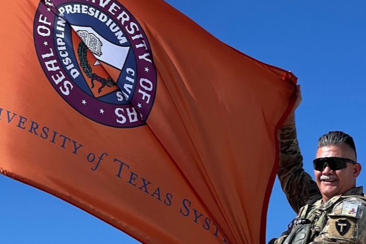 Male veteran in uniform waving orange University of Texas system flag