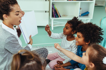 Female childcare teacher holding up a piece of paper, teaching children in a classroom