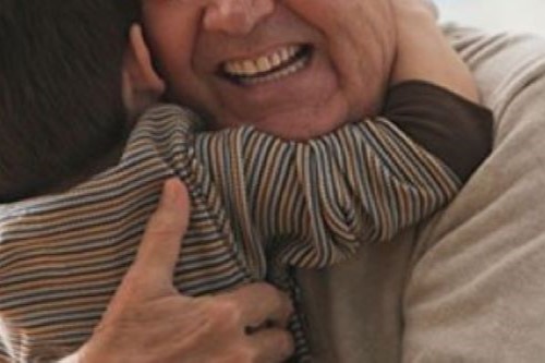 closeup of back of child in striped shirt hugging smiling older man