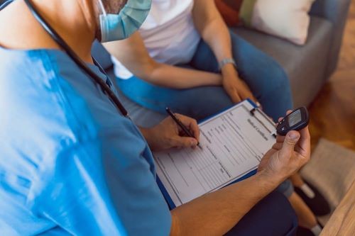 medical worker in mask and scrubs checks off a list on clipboard as patient sits to the side wearing white shirt and jeans