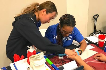 2 UT Southwestern healthcare workers hold patient's hand across table while doing a finger stick blood test