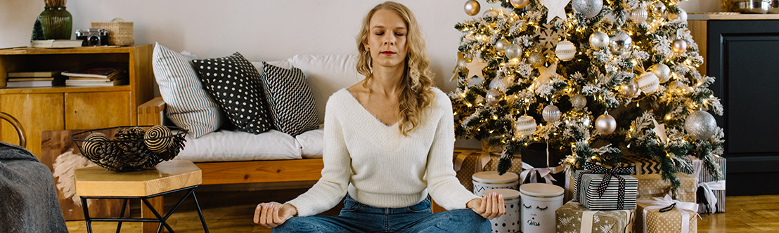 woman with long blonde hair meditating in yoga position on floor in front of Christmas tree