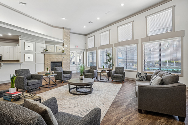 Large room with wall of windows, a fireplace, and rug surrounded by grey fabric sofa and matching armchairs