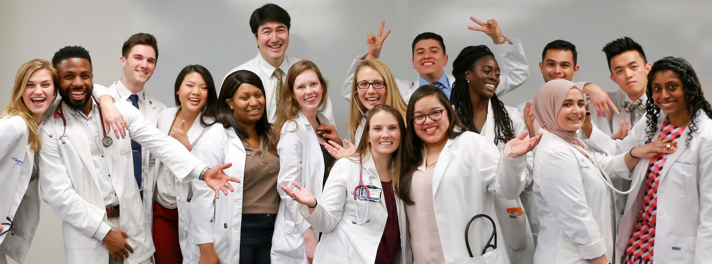 A group of 16 students in white coats