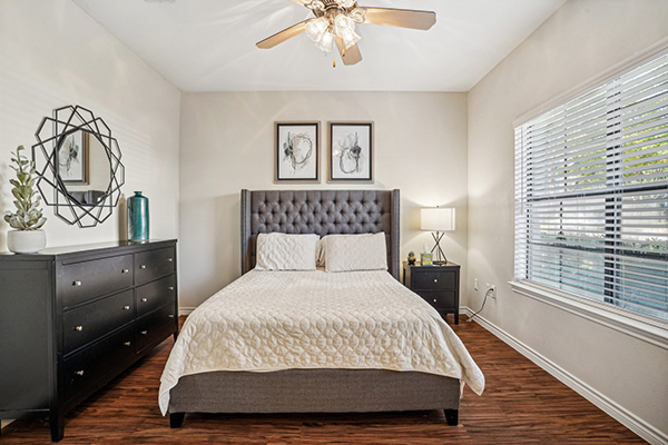 Bed, dresser, and nightstand in a room with a window, ceiling fan light fixture, and wall decor