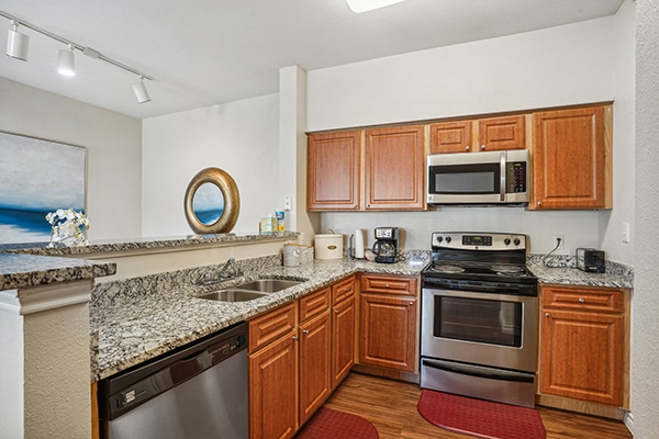 l-shaped kitchen with brown cabinets, double sink, dishwasher, stove and microwave