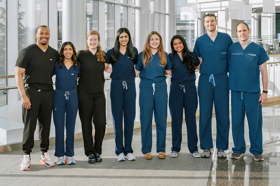 a line of 9 doctors wearing blue scrubs standing in the CUH lobby