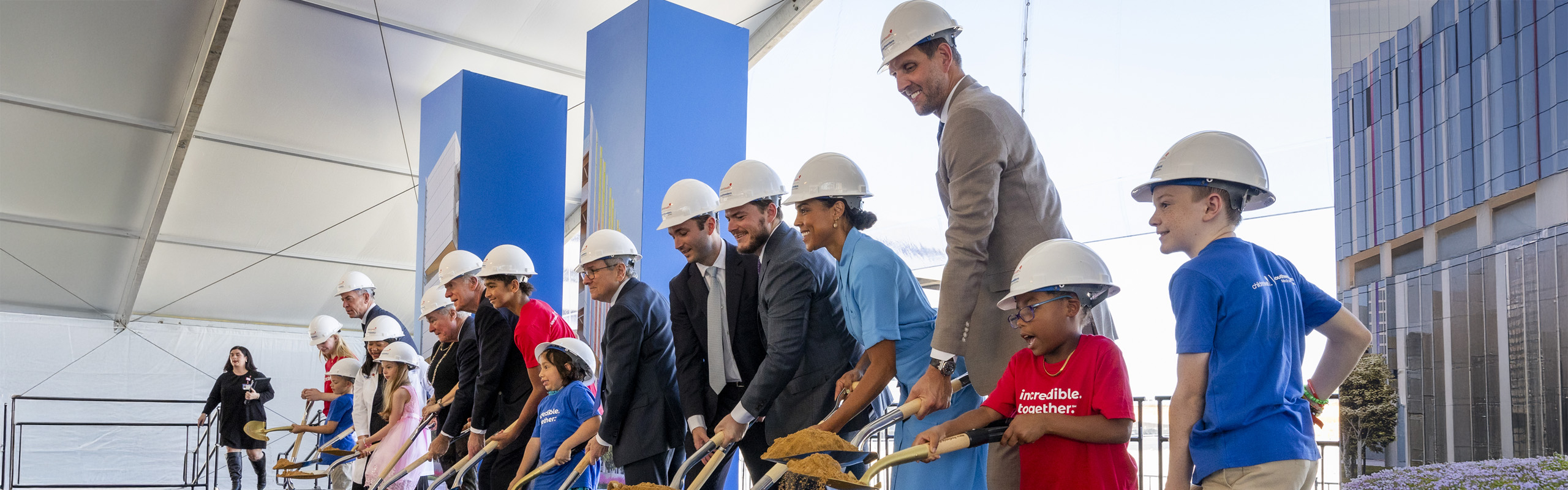 Line of adults and children wearing hardheats and using shovels