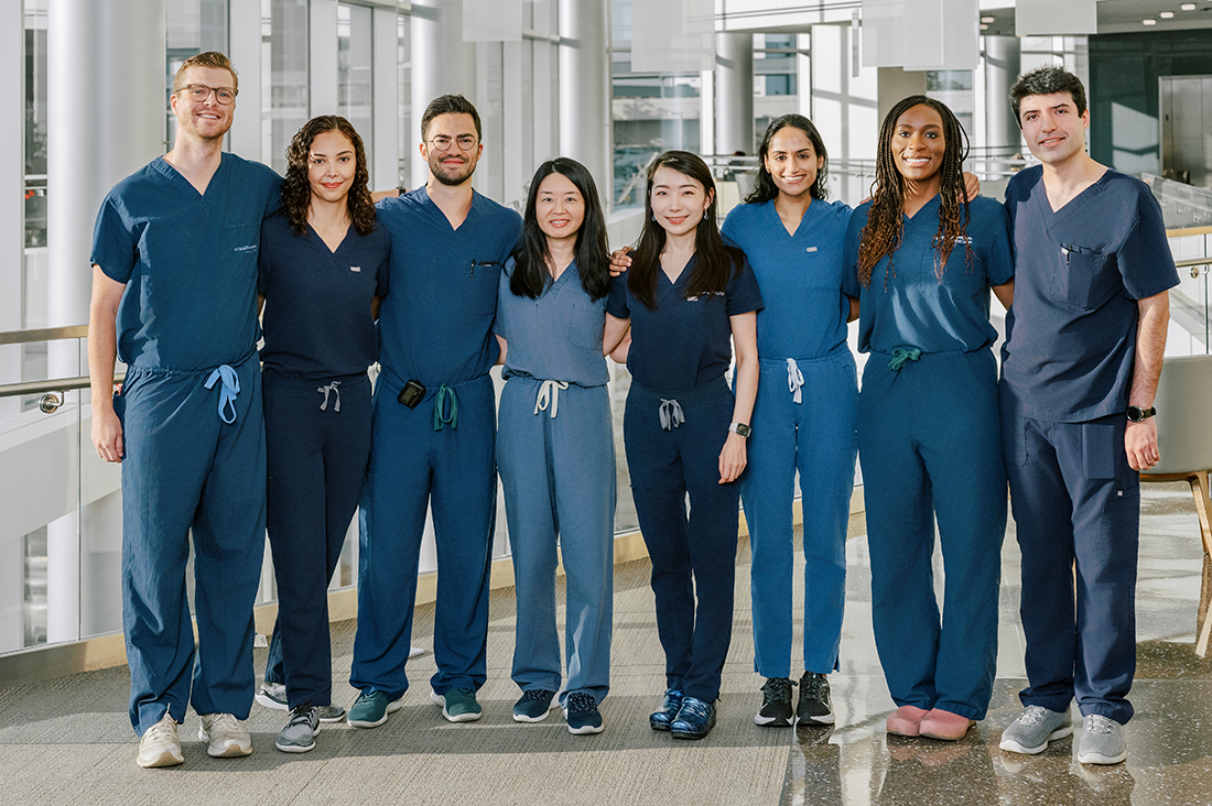 a line of 8 doctors wearing blue scrubs standing in the CUH lobby