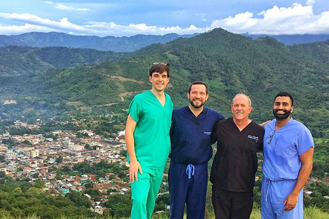 Four people in scrubs on a mountain top overlooking a town