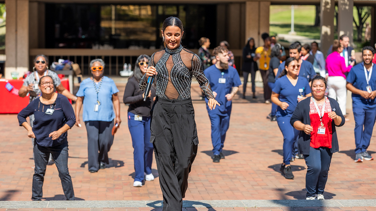 Smiling woman holding a microphone, leading UT Southwestern employees in a dance.