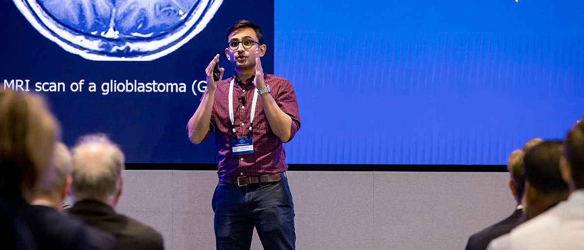 Man on stage in front of screen, speaking to an audience.