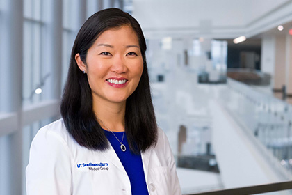 Smiling woman with long black hair, wearing a white UT Southwestern Medical Center lab coat.