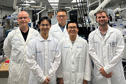 5 men wearing white UT Southwestern lab coats standing in a lab in front of large scientific equipment.