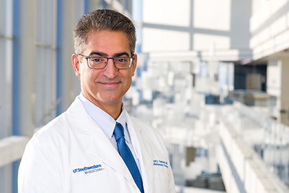 Smiling man with salt-n-pepper hair, wearing a white UT Southwestern Medical Center lab coat, and glasses.