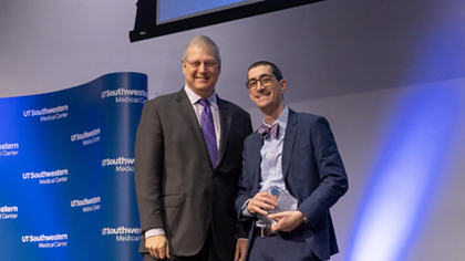 Two men posing. Man on right is holding an award plaque.