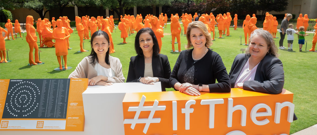 Four women sitting at table in front of a field of orange statues