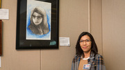 May Urquidi stands beside her self-portrait watercolor, The Moments and a Focus, which was inspired by the environments she is surrounded by each workday.