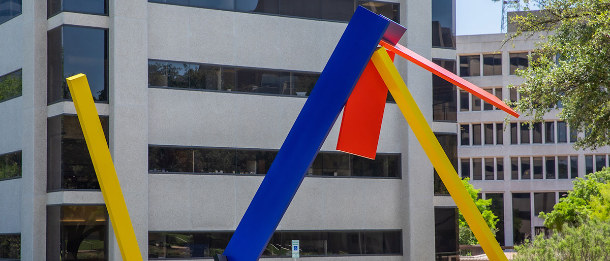 Red yellow and blue metal sculpture surrounded by trees
