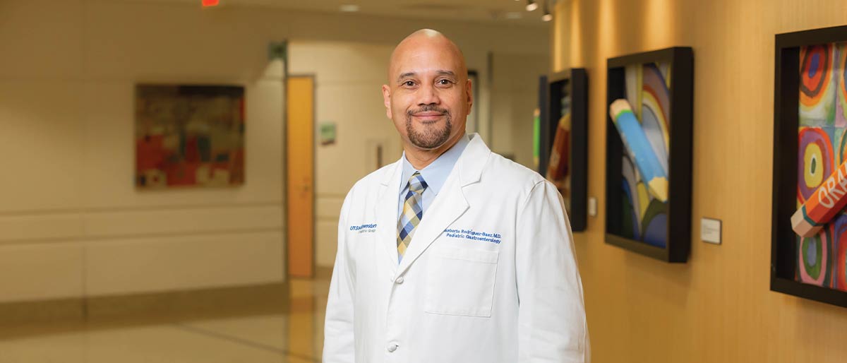 bald man in white lab coat down hall with yellow walls