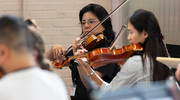 Dr. Feng and Ms. Wang synchronize the sounds of their violins as they follow the sheet music under the conductor’s direction.