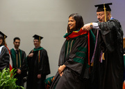 A faculty mentor places a hood over his mentee.