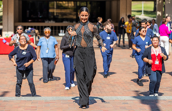 Smiling woman holding a microphone, leading UT Southwestern employees in a dance.