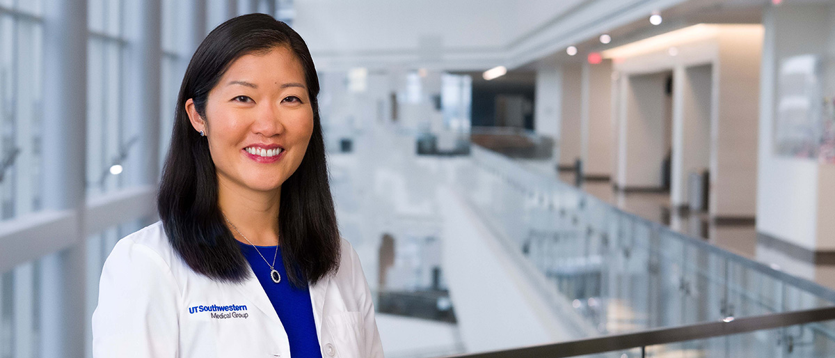 Smiling woman with long black hair, wearing a white UT Southwestern Medical Center lab coat.