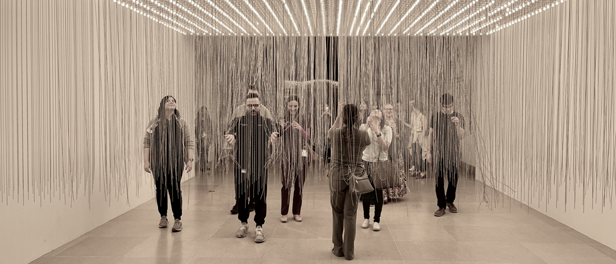 Medical residents visiing a gallery walk through a room with bare light bulbs on the ceiling and hundreds of strings hanging down, nearly reaching the floor.