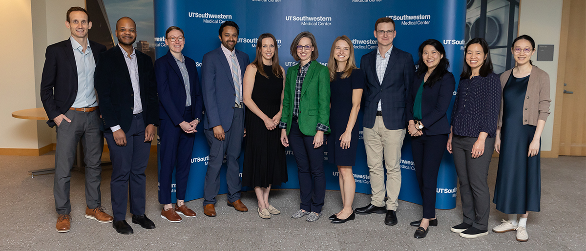 A group of clinical research professionsals pose together in front of a large blue wall with the UT Southwestern Medical School logo.