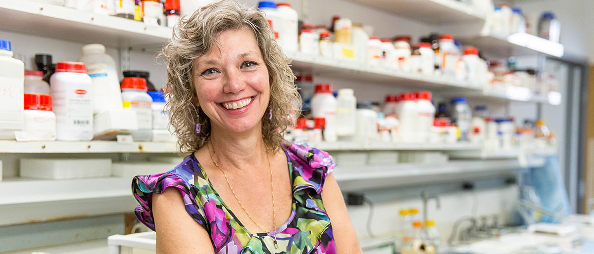 Woman in colorful top in front of shelves in a lab