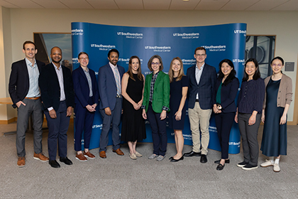 A group of clinical research professionsals pose together in front of a large blue wall with the UT Southwestern Medical School logo.