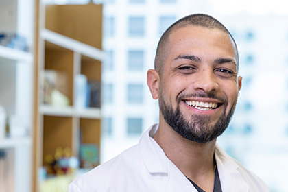 Smiling man with trim dark hair, beard, and mustache, wearing a white UT Southwestern Medical Center lab coat.