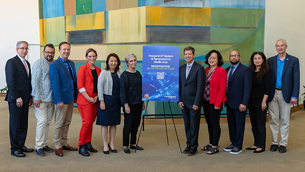 6 men and 5 women gathered in front of a colorful art display with a blue sign on an easle with name of gathering.