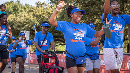 A group of men and women wearing blue UT Southwestern visors and Heart Walk 2024 t-shirts, celebrates crossing the finish line. 