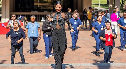 Smiling woman holding a microphone, leading UT Southwestern employees in a dance.