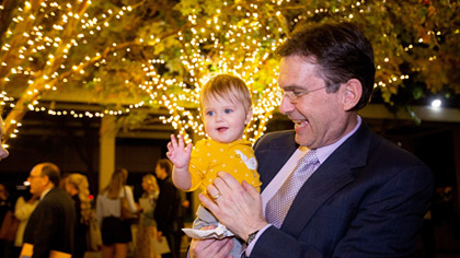 Man holding child in front of trees lined with white lights