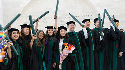 group of graduates in caps and gowns holding up tubes with diplomas
