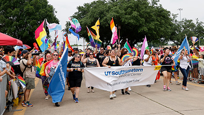 A group of men and women parade down a street carrying brightly colored flags and penants that say, UT Southwestern Medical Center, the future of medicine.