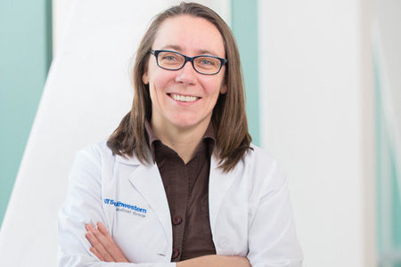 woman with cropped brown hair, glasses, white lab coat, and brown shirt