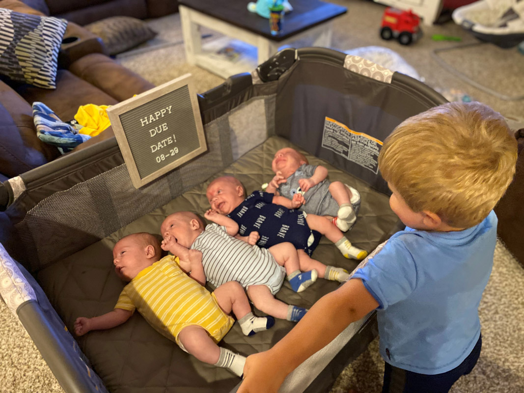 Young boy peeking into crib with four babies