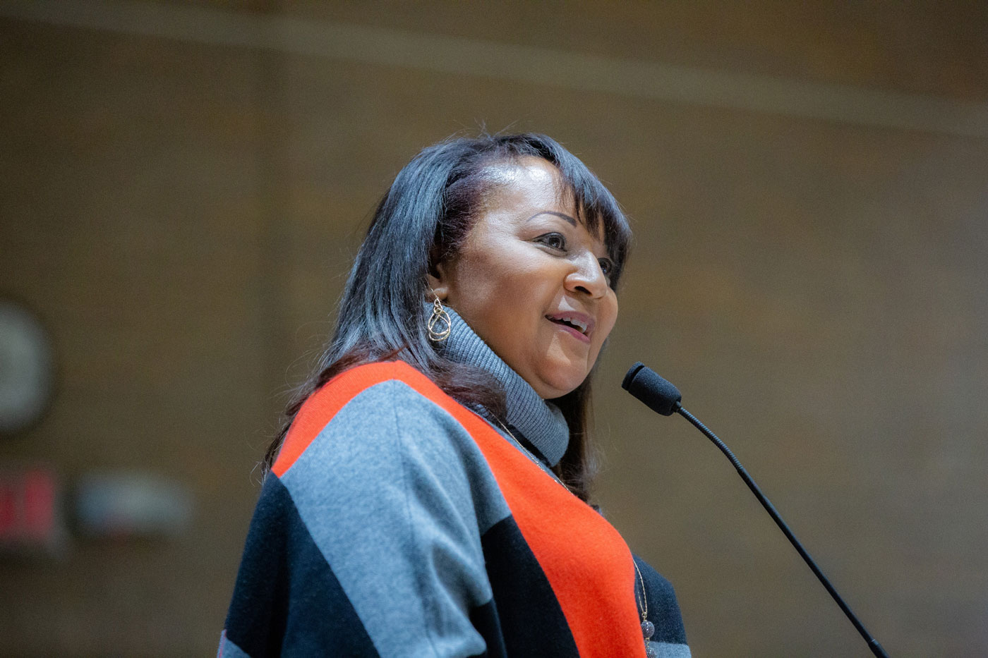 Woman in orange and black top and speaking into mic