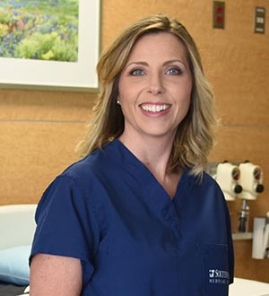 Woman in patient room with blue blond hair, blue UTSW scrub top