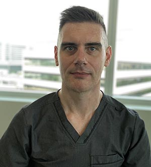 Man with short dark hair, wearing gray scrub top