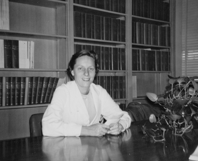 Black and white photo of woman in library wearing white coat