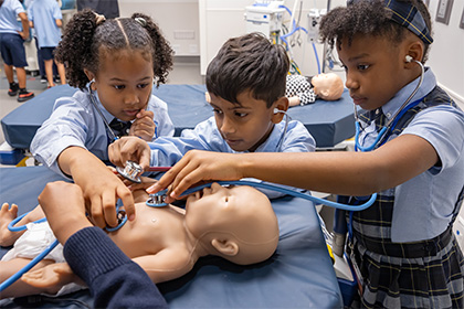 group of 3 kids using stethascope on medical dummy