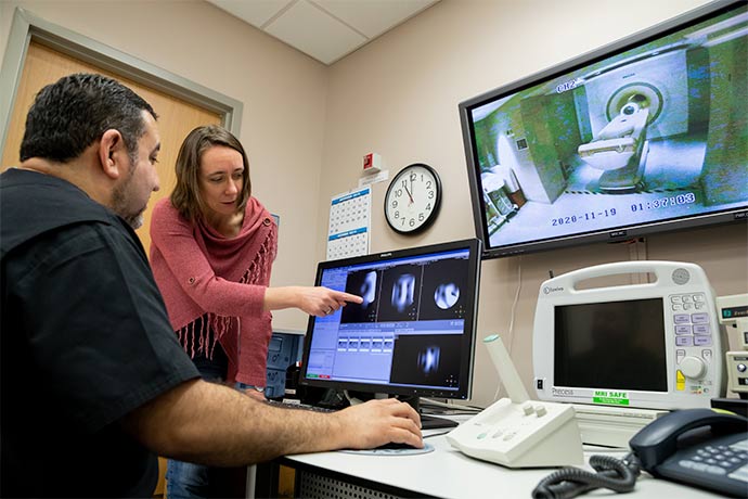 woman in pink shawl sweater and jeans points to computer screen while man in black short sleeved shirt observes